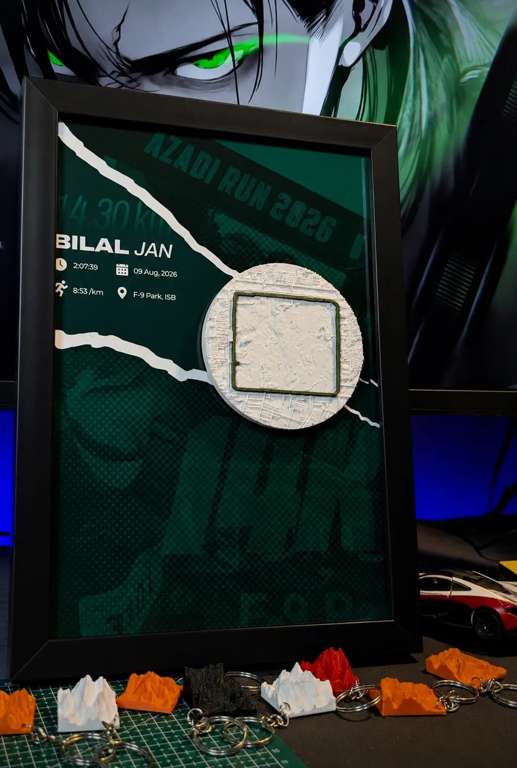 Azadi Run frame standing on the studio desk above a row of terrain keychains