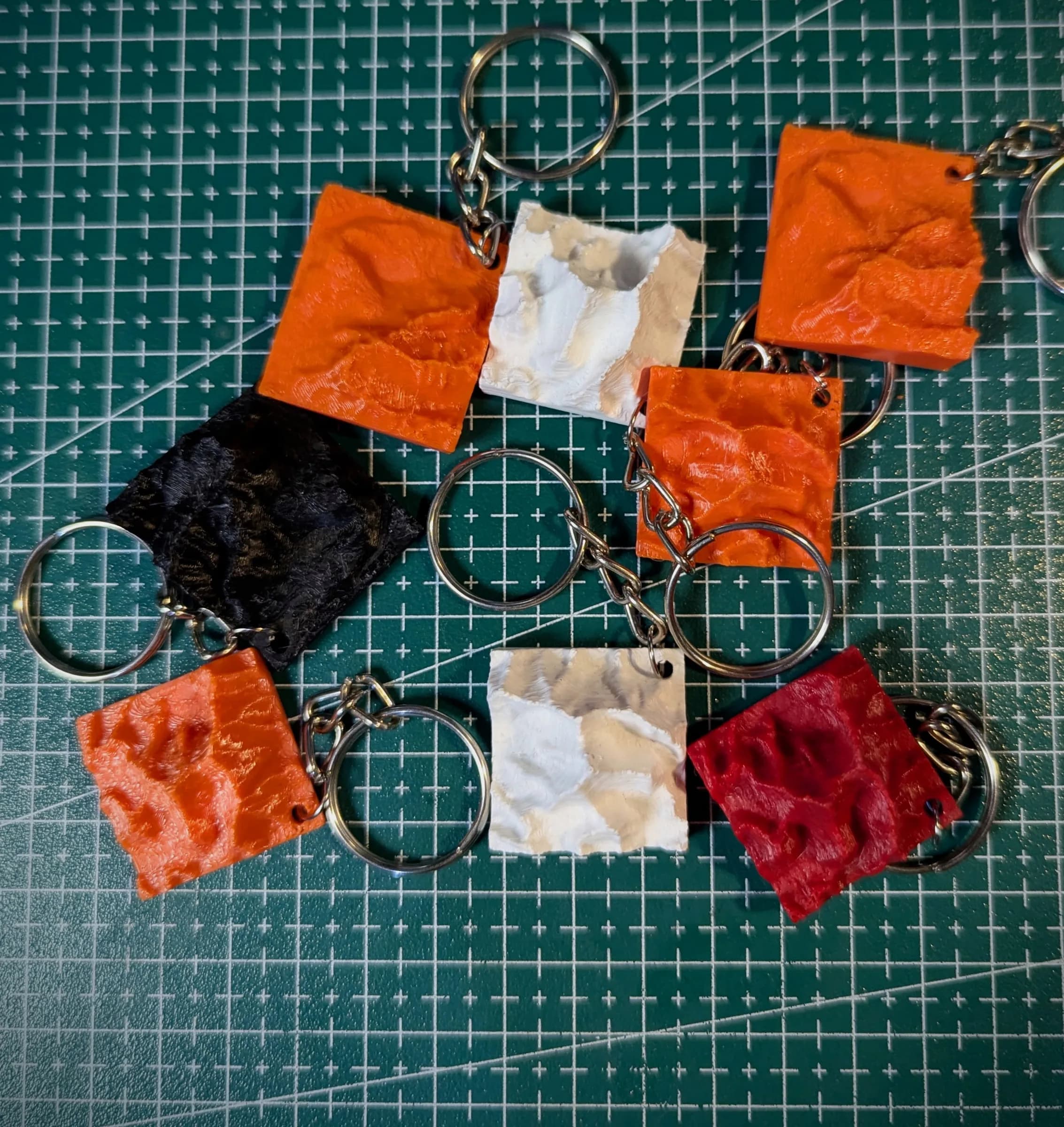 Terrain keychains in orange, red, white and black spread on a cutting mat